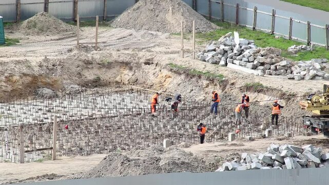 Construction workers in orange vests make a foundation from piles in a monolithic house. Construction of a foundation from reinforcement and piles, industry
