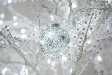 Background delicate glass bauble intricate green floral patterns hangs on white branch glowing bokeh lights. This dreamy and festive background is perfect for holiday and seasonal designs