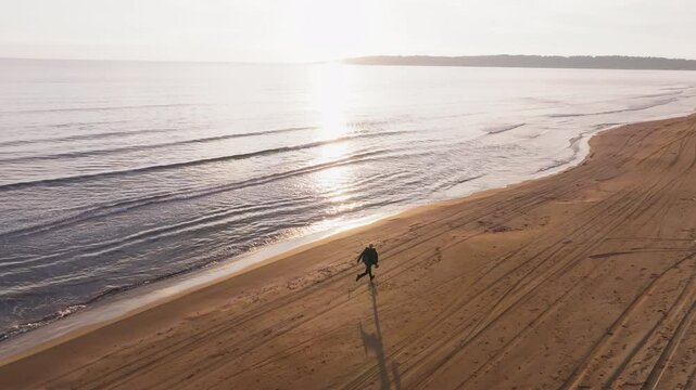 A lone figure runs along Kavouri Beach in Greece at sunset, with waves meeting golden sand