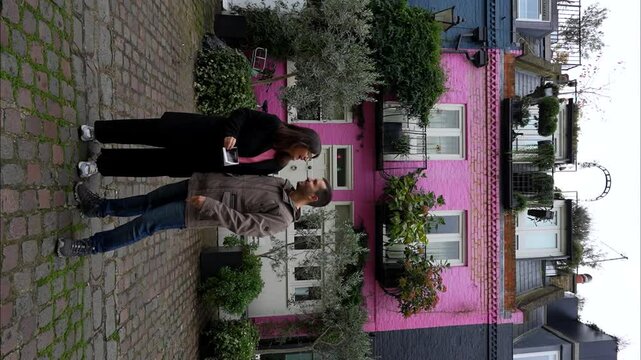 Happy couple showing an ultrasound picture of their future baby in front of a pink house. Vertical