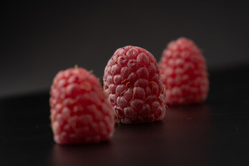 Three raspberries in a row on a black surface with a black background.