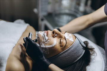 Middle aged woman receiving facial cleansing and care at a cosmetologist office