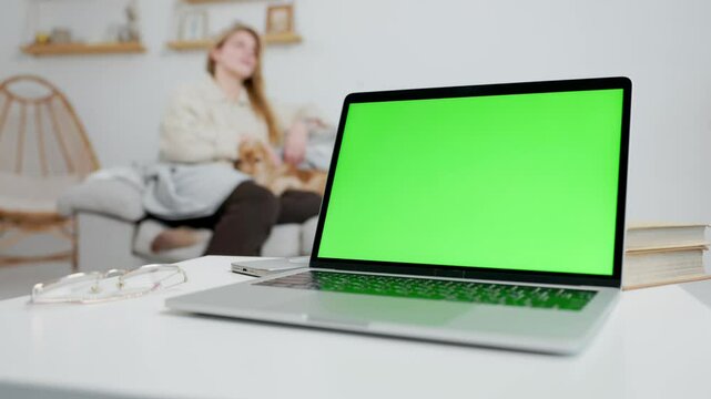 Laptop With Green Mock Up Screen On Table In Home Room With Woman and Her Dog
