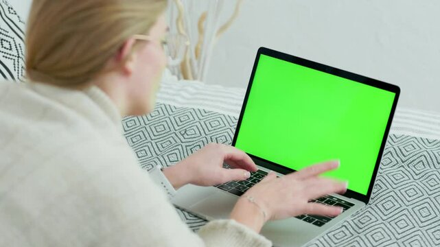 Young Woman In Glasses Using Green Screen Laptop While Lying at Home on Couch. Close up Laptop with Green Mock-up Screen