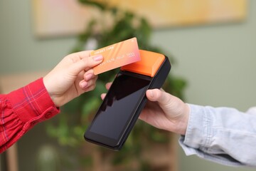 Woman paying with credit card via terminal against blurred background, closeup