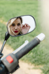 Woman with Red Lipstick Looking into Motorcycle Mirror. A woman with red lipstick gazes into a black and silver motorcycle mirror. Perfect for themes of reflection, biker style, and modern fashion