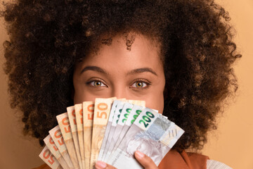 joyful black woman showing money, brazilian Real in beige background. financial, credit, purchase,...