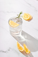 Glass of fresh drink with lemon and rosemary on white background. Cold lemonade or water on a bright sunny day. 