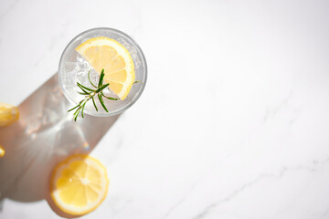 Top view of fresh summer drink - water, lemonade with lemon, rosemary and ice in a glass. Top view,...