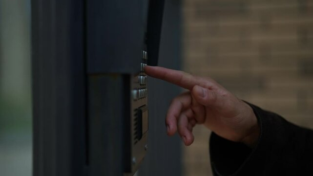 Close-up hands of unrecognizable man ringing intercom system standing on urban street, waiting for access to residential building. Concept of modern technology connecting visitors to secure entrances.