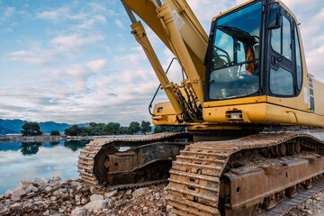 Heavy Yellow Excavator on Rocky Terrain at a Coastal Construction Site with Calm Water