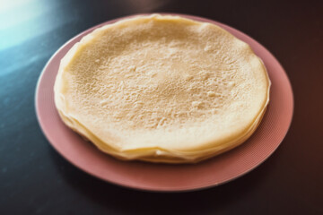 Stack of Thin Homemade Crepes on a Pink Striped Plate with a Soft Focus Background