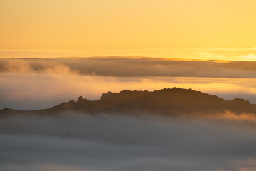 A rural sunrise winter landscape of Ramshaw Rocks shrouded in mist and fog during a cloud inversion in the Staffordshire Peak District National Park, England, UK.