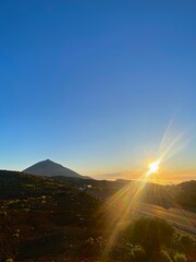 The evening sun sinks under the mountain next to the silhouette of a big volcano