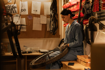 Female cycling mechanic checking bicycle wheel in workshop. Bike service, repair and upgrade