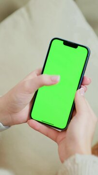 Mobile Phone With Green Mock Up Screen In Female Hands Close Up. Vertical Video