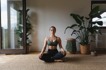 Woman sitting cross-legged and meditating on rug at home