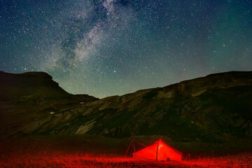 Illuminated tent near mountain under Milky Way