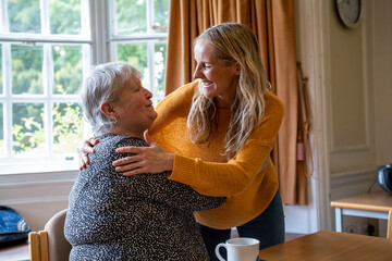 Happy caregiver embracing senior woman at retirement community