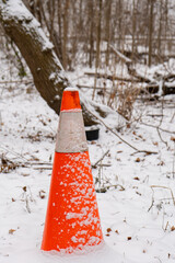 A "Stop" sign and road cone indicating caution near a river in a winter park, surrounded by snow.