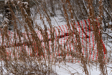A bright orange warning barrier near a snow-covered river, with a stretched mesh to prevent entry.