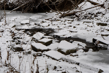 Snow-covered rocks and a river in the forest during winter, surrounded by natural beauty.
