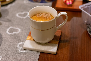 White coffee cup with a heart design sits on a coaster on a wooden table. The heart design on the...