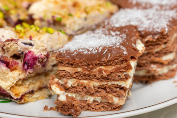 Plate of desserts with a piece of chocolate cake on top. The cake is covered in chocolate and has a white frosting. There are also other desserts on the plate, including a piece of cake with nuts