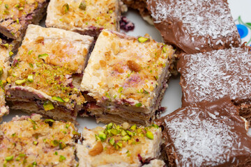 Plate of desserts with a piece of chocolate cake on top. The cake is covered in chocolate and has a white frosting. There are also other desserts on the plate, including a piece of cake with nuts