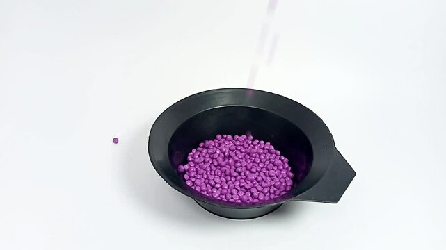 Violet color masterbatch flowing contained in cup, various polymer masterbatch plastic granules carrying color pigment, isolated on pink background, for industrial plastic product videography design