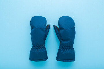 Pair of new dark blue waterproof warm winter mittens for kid on light blue table background. Pastel color. Closeup. Top down view.