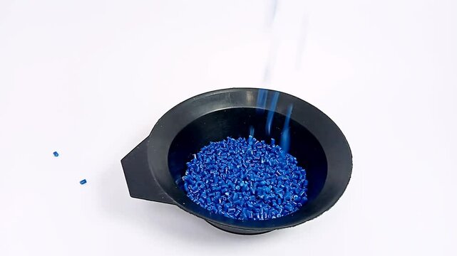 blue color masterbatch flowing contained in cup, various polymer masterbatch plastic granules carrying color pigment, isolated on white background, for industrial plastic product videography design