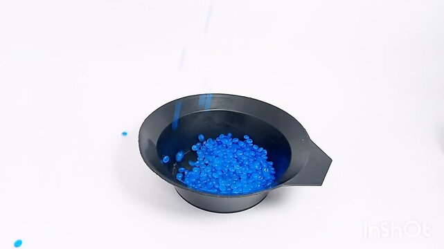 blue color masterbatch flowing contained in cup, various polymer masterbatch plastic granules carrying color pigment, isolated on white background, for industrial plastic product videography design