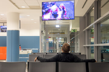 A lone passenger is watching a sports broadcast on television at a night airport