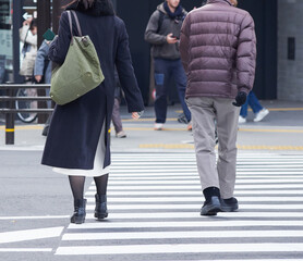 冬の都市の交差点の横断歩道を渡る通勤中の若い女性と人々の姿