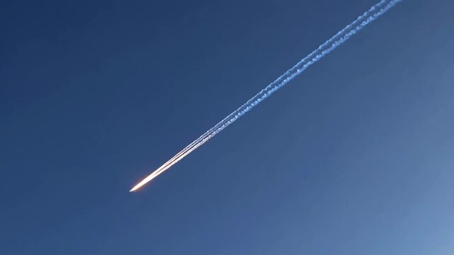 Commercial airplane with contrail streak across deep blue sky. Red glow from aircraft against azure background. Aviation and air travel concept for transportation design with copy space
