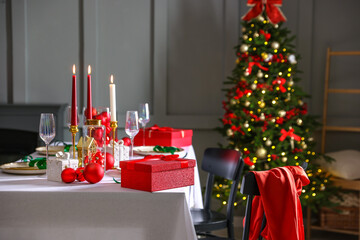 Christmas table setting with stylish dishware, glasses and burning candles in festive decorated room