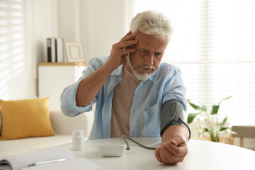 Senior man measuring blood pressure at table indoors