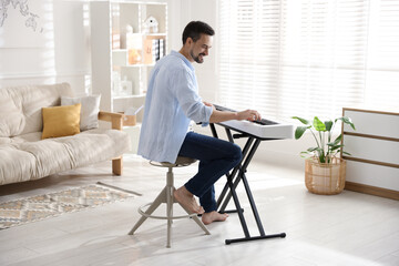 Smiling man playing synthesizer at home. Electronic musical instrument