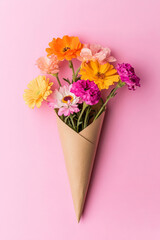 A small bouquet of fresh flowers wrapped in kraft paper, arranged on a soft pink background. The minimalist and elegant flat-lay composition makes it ideal for romantic or celebratory themes.