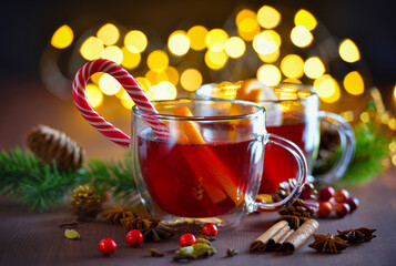 Two glass of christmas mulled wine or gluhwein with spices and orange slices against the background of festive lights. Traditional hot drink at Christmas time
