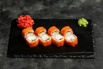 Sushi rolls, red pickled ginger and wasabi on black tray