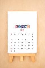 Calendar page for March 2025 with wood easel on old brown background.