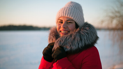 photo with a young woman in the winter forest. girl in a snowy park. in a red jacket on the banks of a frozen river. winter walk in nature. Cold season. Beautiful girl, sunny day. soft focus