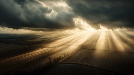 Dramatic sunset over wind turbine farm illuminating agricultural fields with striking rays of light through dark clouds