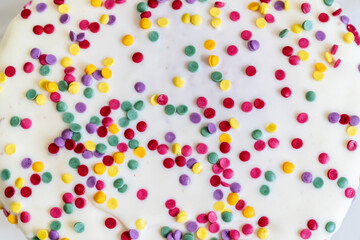 Closeup of white frosted cake topped with colorful sprinkles. Macro photography of dessert decoration. Celebration and festive dessert concept.