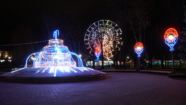 A night amusement park. Illuminated fountain on the background of a ferris wheel.