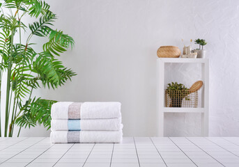 White and grey towels in a row, vase of plant background with bath room objects cabinet.