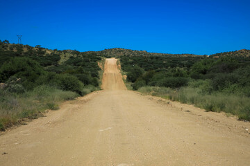 Endless and sandy gravel road through the desert in the beautiful Kalahari National Park. Tourism and vacation concept. Namibia, Africa.