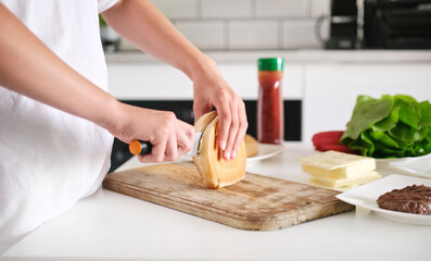 Little Girl Cutting A Bun For A Meat Burger While Cooking In The Kitchen